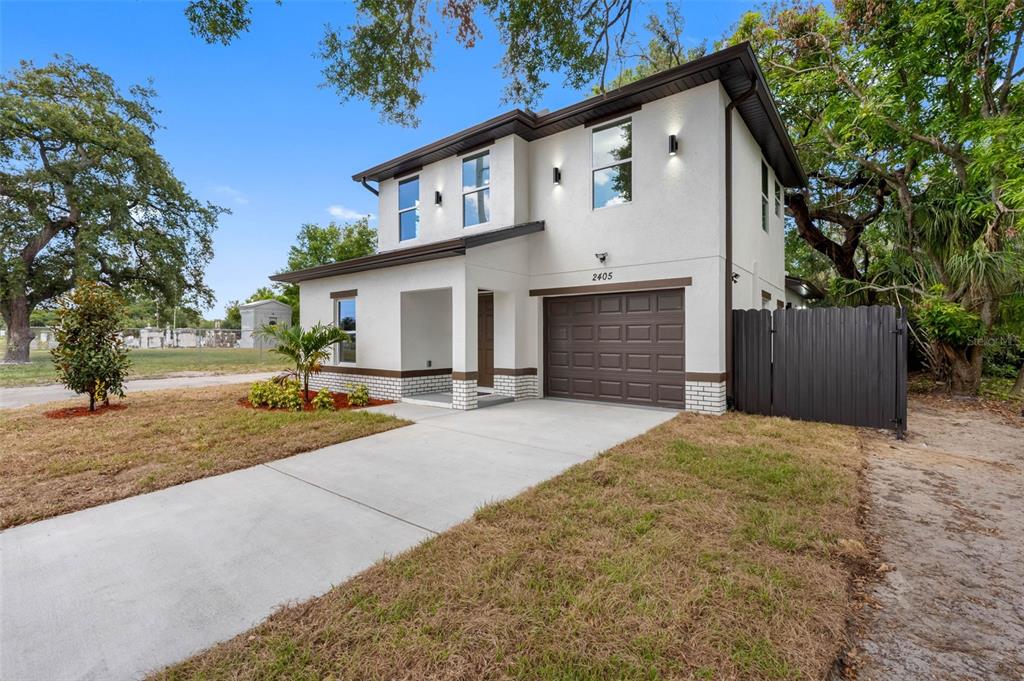 A two-story white stucco house features a brown garage door and a concrete driveway — 2405 E 23RD AVENUE, TAMPA, FL