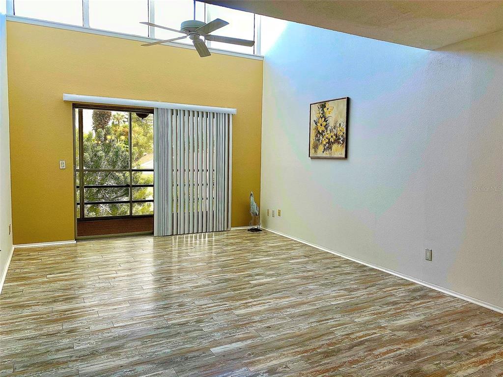 A living room features wood-look flooring, a vaulted ceiling, and a sliding glass door — 729 CAPRI ISLES BOULEVARD UNIT 216, VENICE, FL