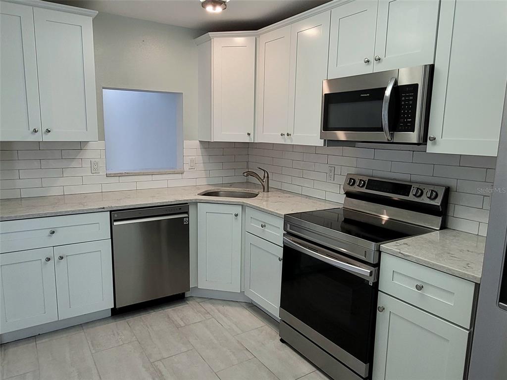 A kitchen features white cabinets, stainless steel appliances, a subway tile backsplash, and light countertops — 729 CAPRI ISLES BOULEVARD UNIT 216, VENICE, FL