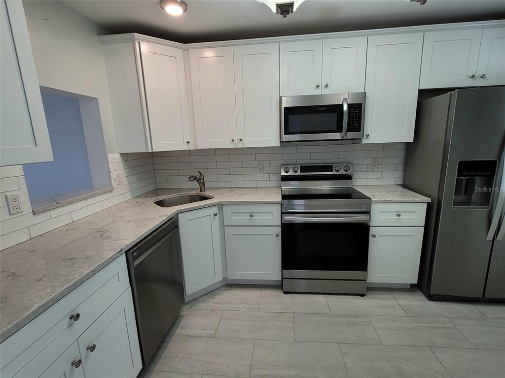 A kitchen features white cabinets, stainless steel appliances, a subway tile backsplash, and stone countertops — 729 CAPRI ISLES BOULEVARD UNIT 216, VENICE, FL