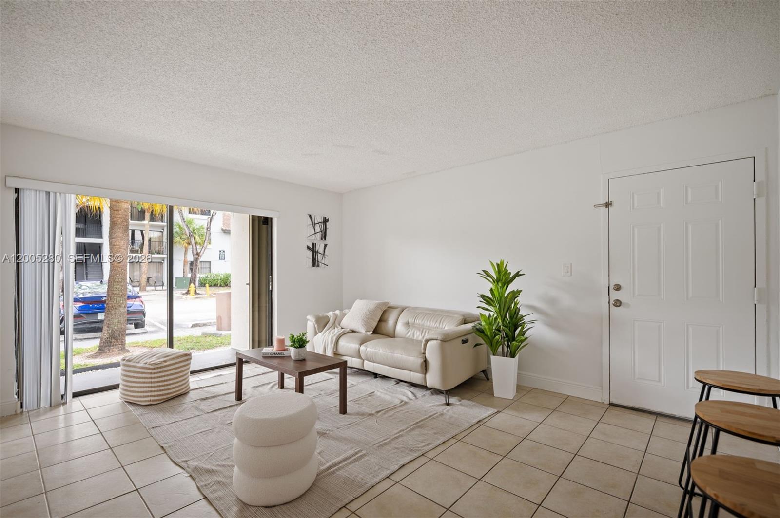A living room features white walls, tile flooring, a beige sofa, and a sliding glass door — 7195 NW 179th St # 106, Hialeah FL 33015, HIALEAH, FL