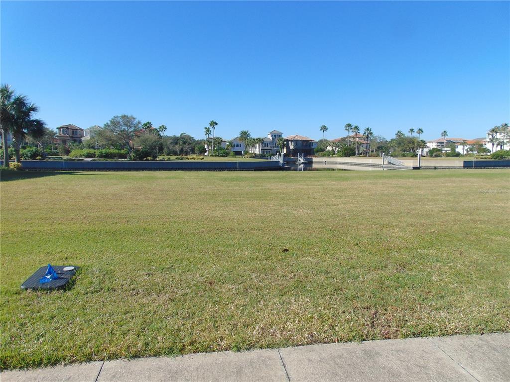 A wide, grassy vacant lot overlooks a canal with houses in the background — 258 HARBOR VILLAGE POINT N, PALM COAST, FL