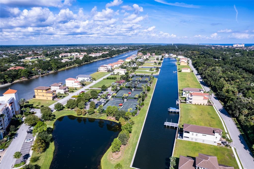 An aerial view shows a residential community with a canal, tennis courts, and a pond — 258 HARBOR VILLAGE POINT N, PALM COAST, FL