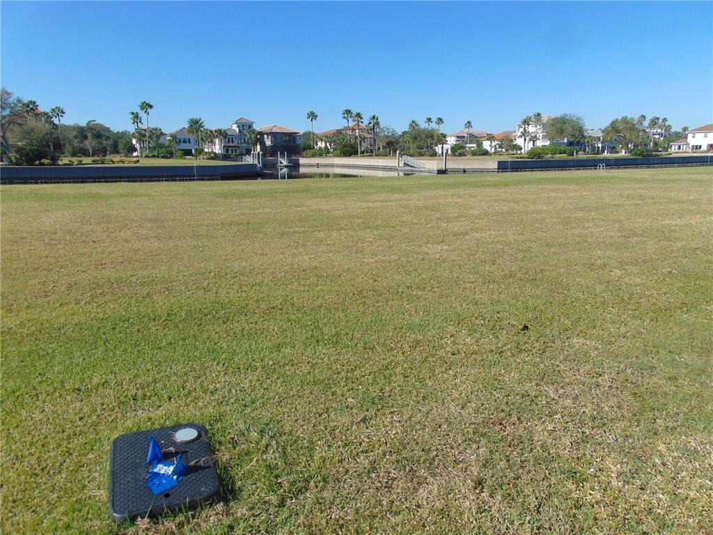 A large, grassy vacant lot overlooks a canal with houses in the background — 258 HARBOR VILLAGE POINT N, PALM COAST, FL