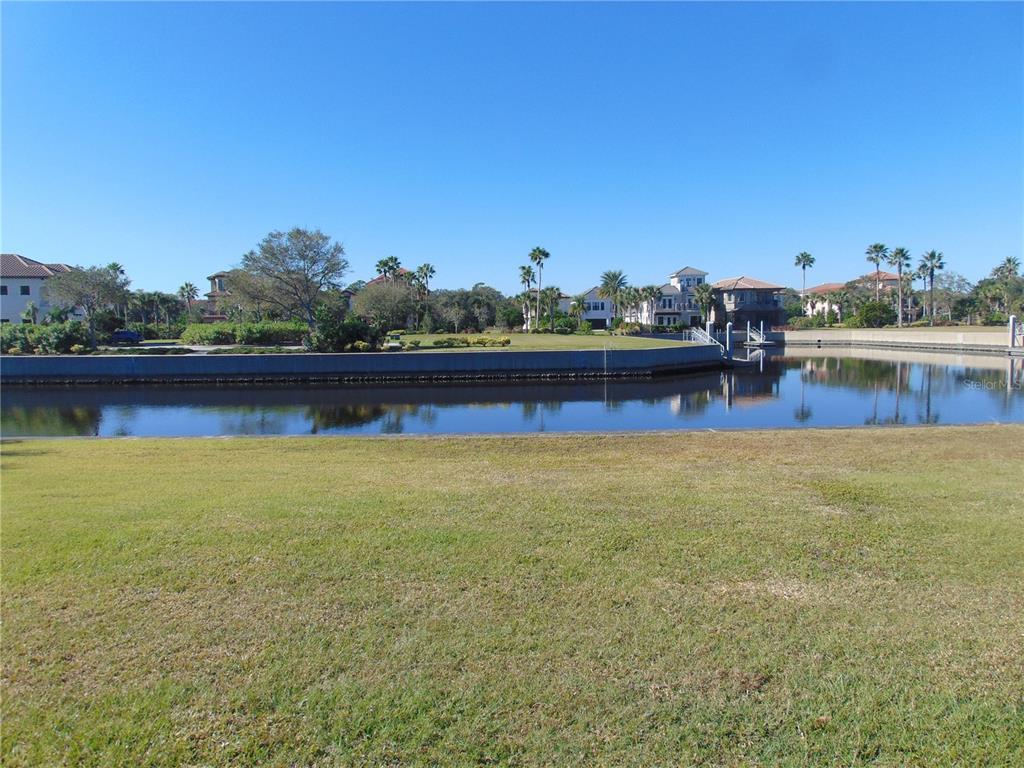A grassy lawn overlooks a calm canal with a concrete seawall and distant residential homes — 258 HARBOR VILLAGE POINT N, PALM COAST, FL
