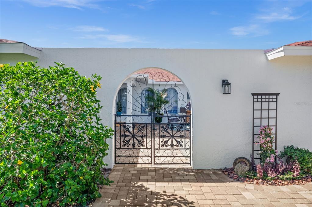 A white stucco wall features an arched gate leading to a private courtyard entrance — 1432 VENETIAN COURT, CAPE CORAL, FL
