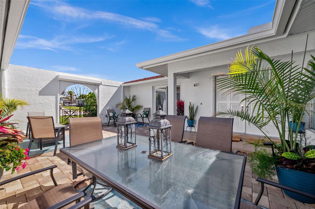 A glass-topped dining table sits on a paved patio with outdoor chairs and potted plants — 1432 VENETIAN COURT, CAPE CORAL, FL