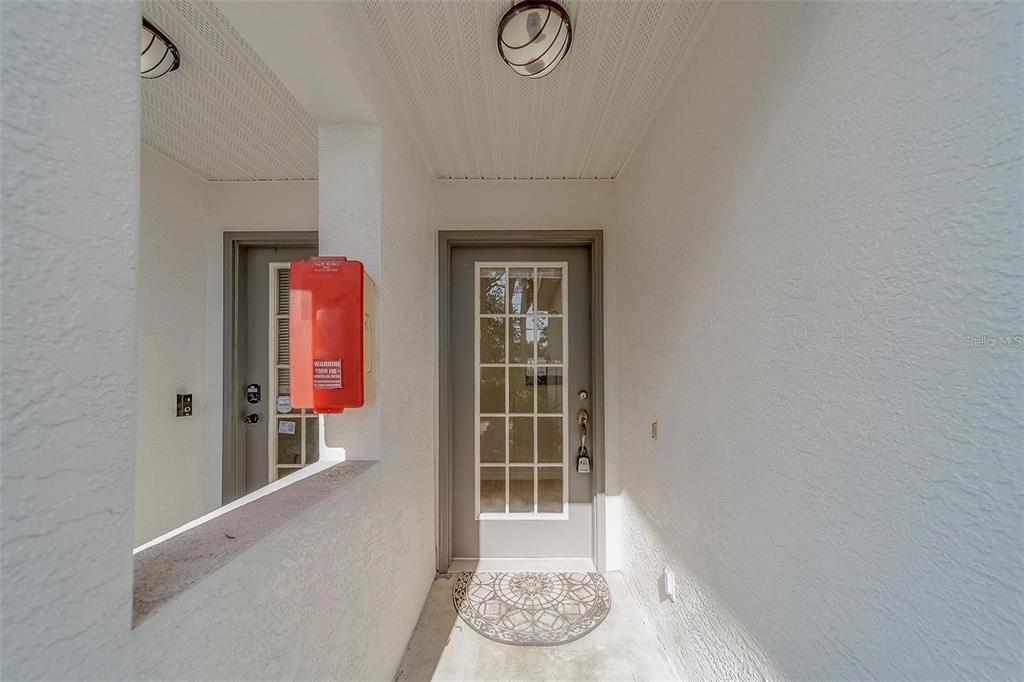 A covered entryway features a gray door with glass panes and a red fire extinguisher — 9209 JAKES PATH, LARGO, FL