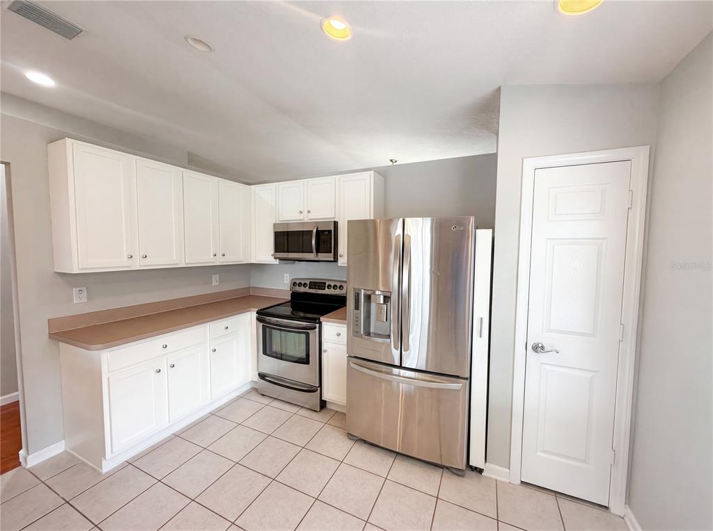 A kitchen features white cabinets, stainless steel appliances, tan countertops, and light-colored tile flooring — 575 SEA HOLLY DRIVE, BROOKSVILLE, FL