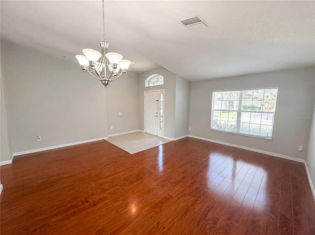 An empty room features hardwood floors, a chandelier, and a tiled entryway by the door — 575 SEA HOLLY DRIVE, BROOKSVILLE, FL