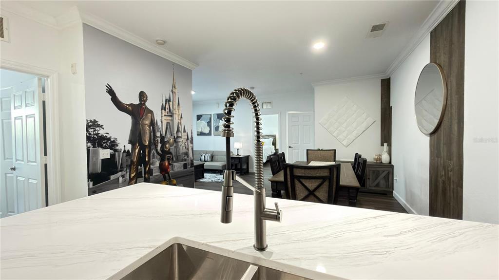 A kitchen island with a metal faucet overlooks a dining area and a Disney-themed mural — 1301 TUSCAN TERRACE UNIT 9403, DAVENPORT, FL