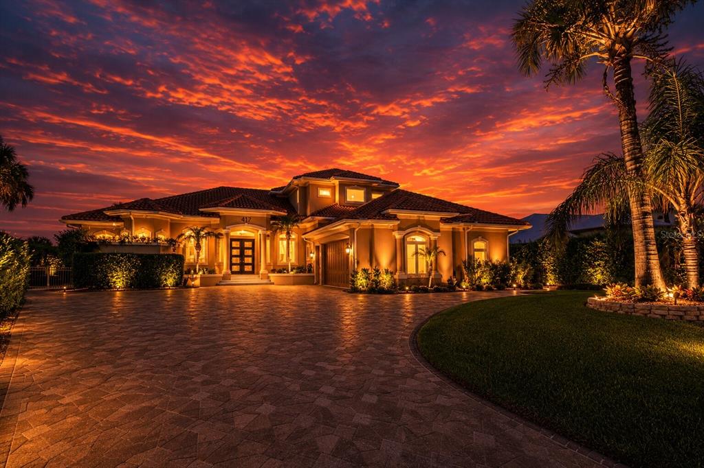 A large Mediterranean-style house with a paved driveway and palm trees under a sunset sky — 417 QUAY ASSISI, NEW SMYRNA BEACH, FL