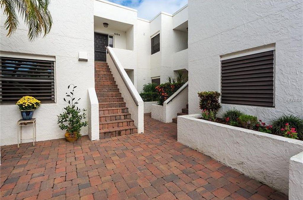 An exterior view of a white stucco building with brick stairs and a brick patio — 5154 MARSH FIELD LANE UNIT 118, SARASOTA, FL