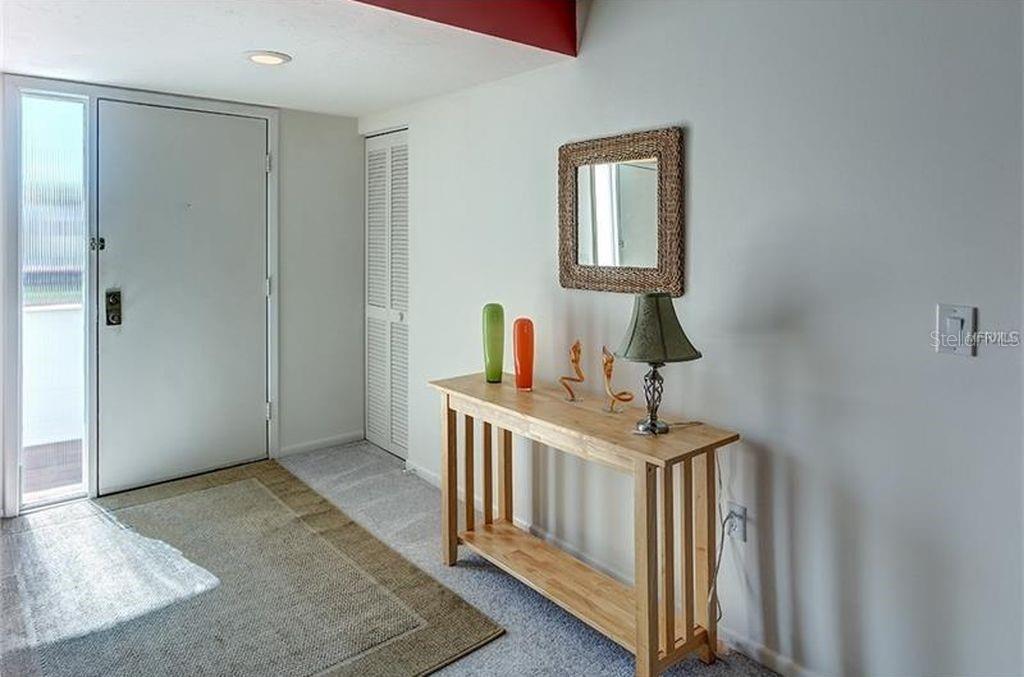 An entryway features a light wood console table, a mirror, and a white front door — 5154 MARSH FIELD LANE UNIT 118, SARASOTA, FL