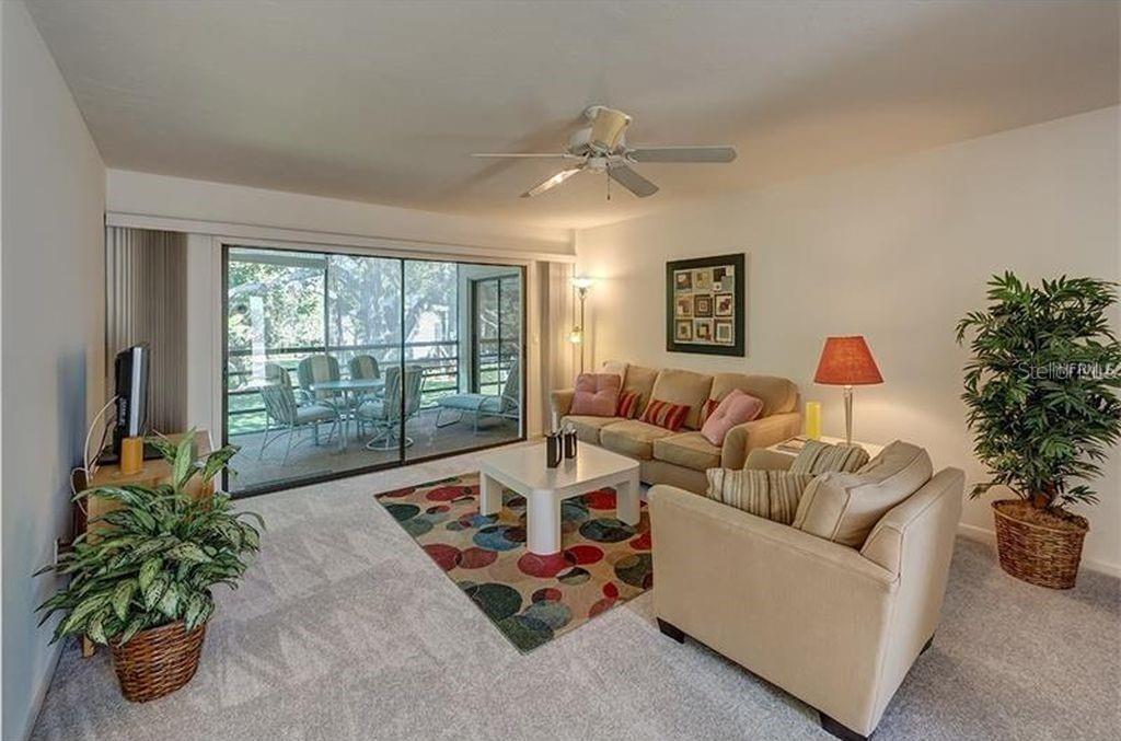 A living room with beige furniture, a colorful patterned rug, and a sliding glass door — 5154 MARSH FIELD LANE UNIT 118, SARASOTA, FL
