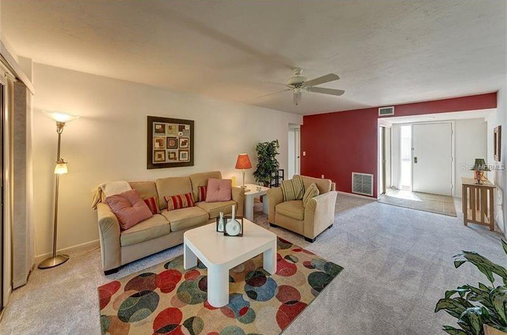 A living room features a beige sofa, matching armchair, patterned area rug, and red accent wall — 5154 MARSH FIELD LANE UNIT 118, SARASOTA, FL