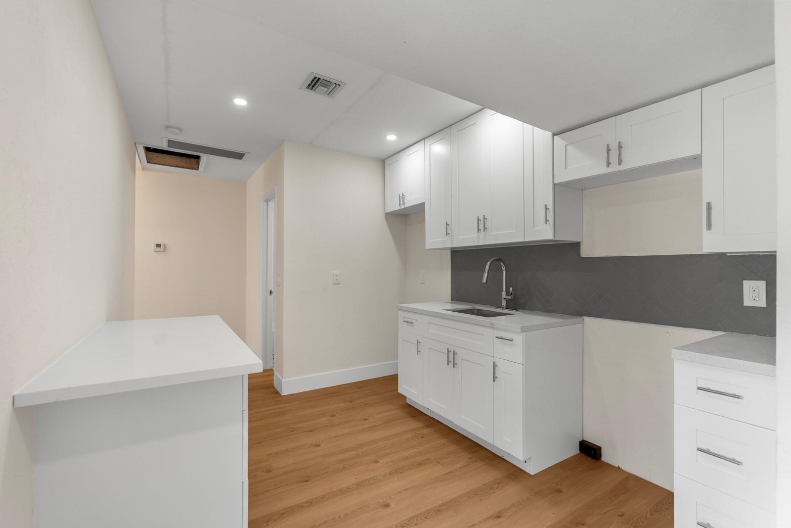 A kitchen features white cabinets, a grey herringbone backsplash, and light wood-look flooring — 865 SE 12th Street # A, Hialeah FL 33010, HIALEAH, FL