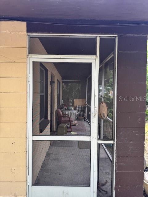 A white screen door opens to a covered porch with concrete flooring and outdoor furniture — 8609 N 13TH STREET, TAMPA, FL