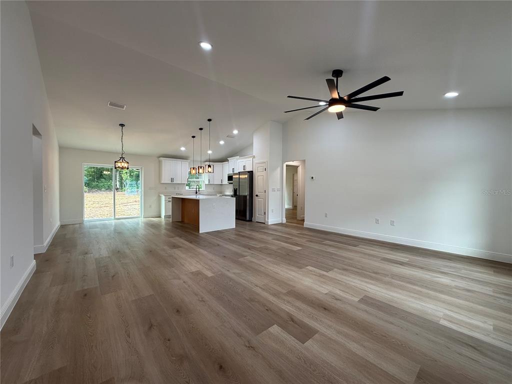 An open-concept living area features light wood-look flooring, a kitchen with an island, and a ceiling fan — 3641 SE 140TH PLACE, SUMMERFIELD, FL