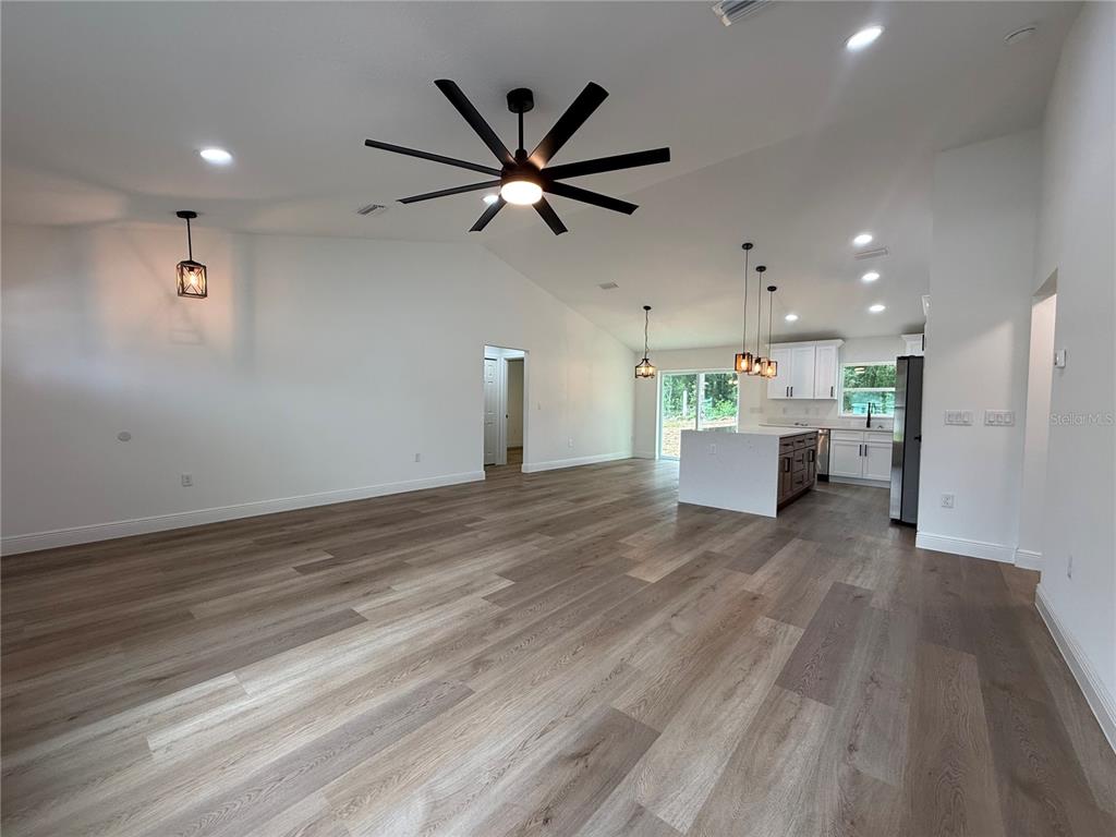 An open-concept living area features wood-look flooring, a large ceiling fan, and a modern kitchen — 3641 SE 140TH PLACE, SUMMERFIELD, FL