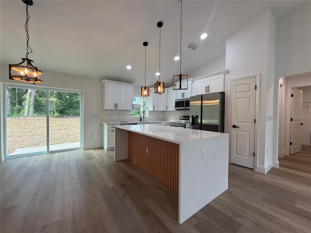 A modern kitchen features white cabinetry, a quartz-topped island with wood slats, and pendant lighting — 3641 SE 140TH PLACE, SUMMERFIELD, FL