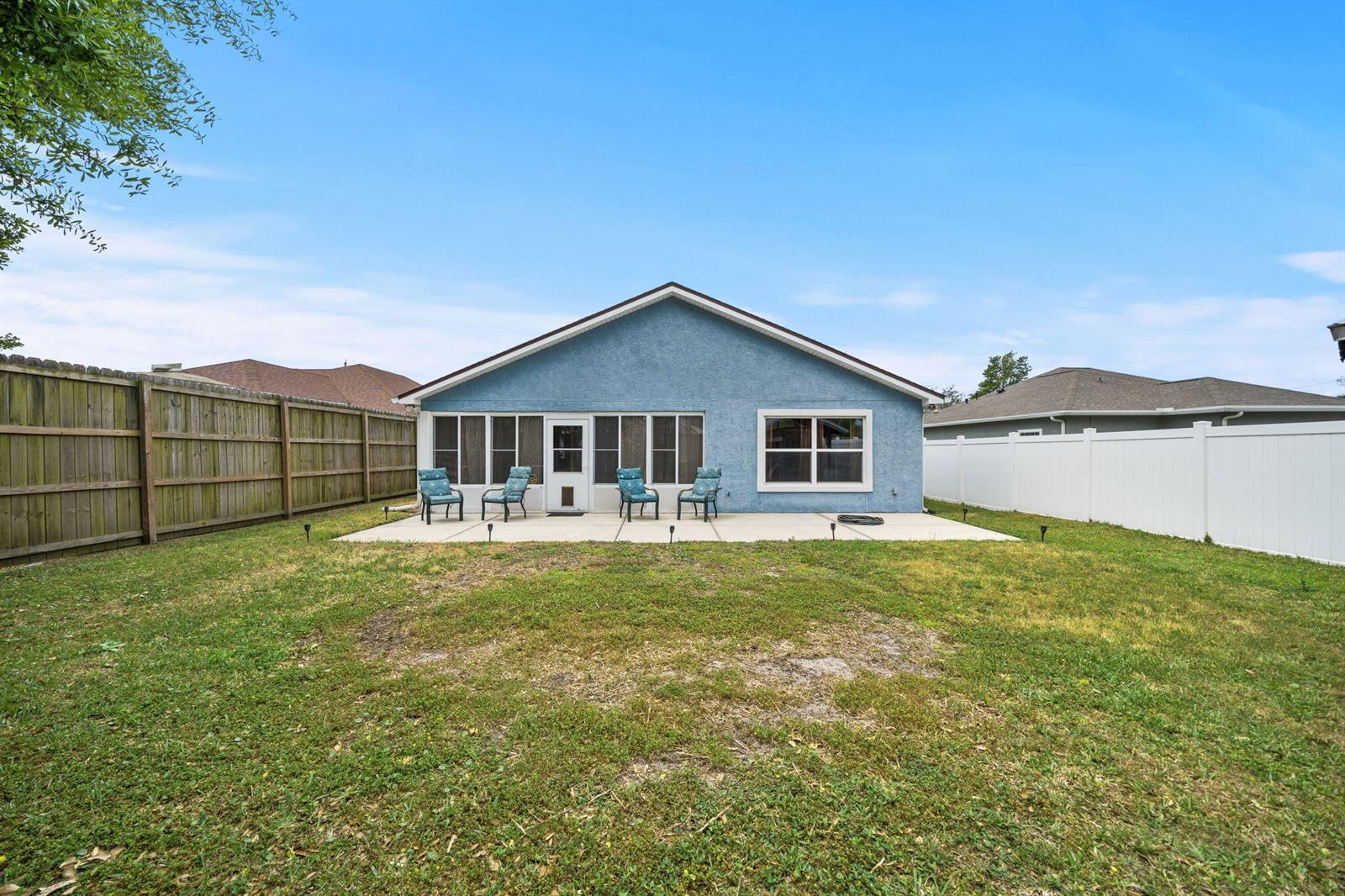 The backyard features a blue stucco house with a concrete patio and a screened porch — 1407 Rhode Island Avenue, FL 32444, FL