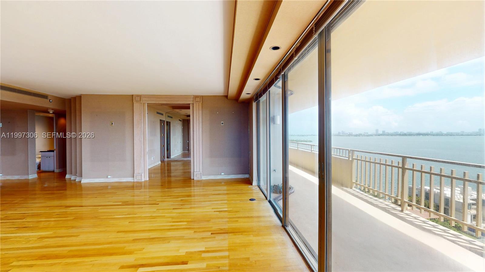 An empty room with hardwood floors features a wall of sliding glass doors overlooking water — 11113 Biscayne Blvd # 1251, Miami FL 33181, MIAMI, FL