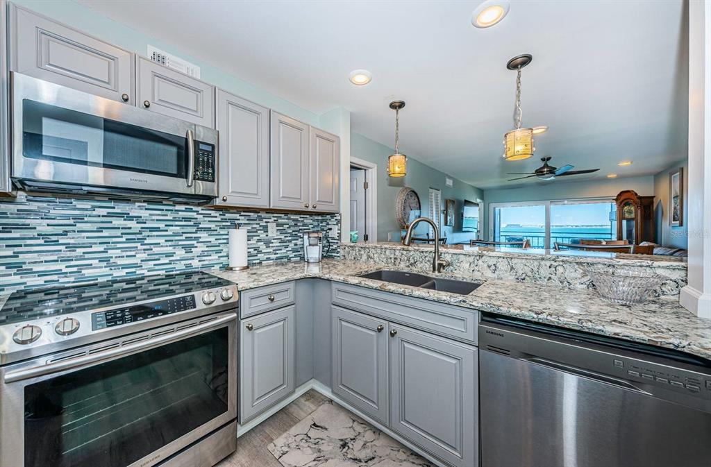 A kitchen with gray cabinets, granite countertops, stainless steel appliances, and a glass tile backsplash — 6265 SUN BOULEVARD UNIT 309, ST PETERSBURG, FL