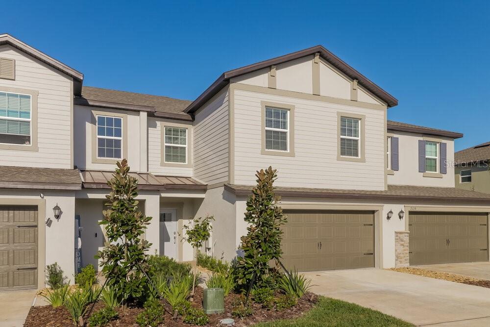 A two-story townhouse with beige siding, a tan garage door, and a small front garden — 2123 CERULEAN SKY DRIVE, LUTZ, FL