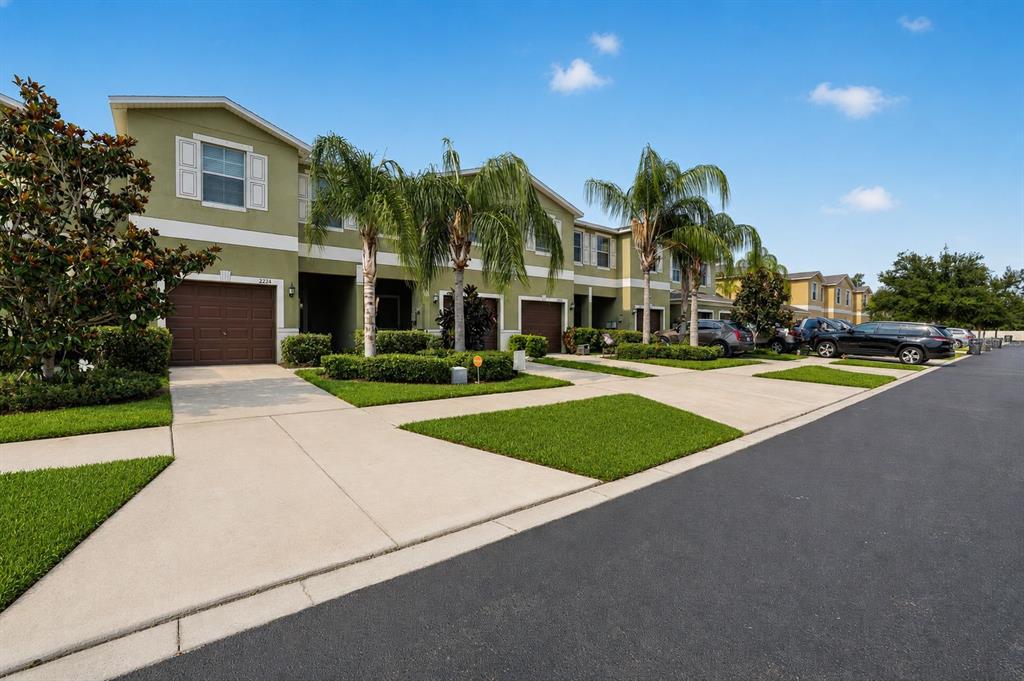 A row of two-story townhomes with green stucco facades, attached garages, and palm trees — 2224 GOLDEN FALCON DRIVE, RUSKIN, FL