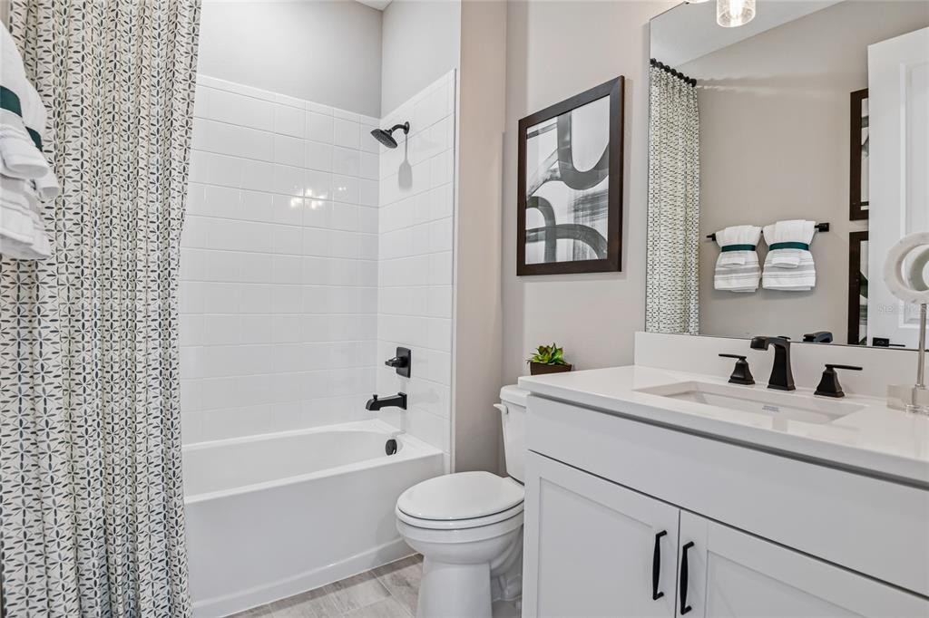 A bathroom features a white vanity, a toilet, and a shower-tub combo with white tiles — 6398 CLOVER STREET, LAKE HAMILTON, FL