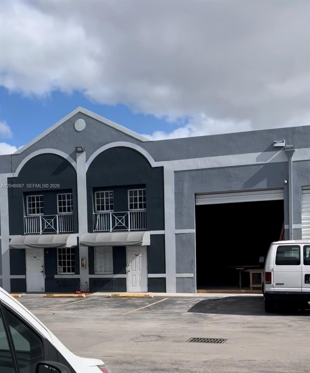A two-story commercial building features gray stucco walls, arched architectural details, and a large bay door — 10680 NW 123rd St Rd # 104, Medley FL 33178, MEDLEY, FL