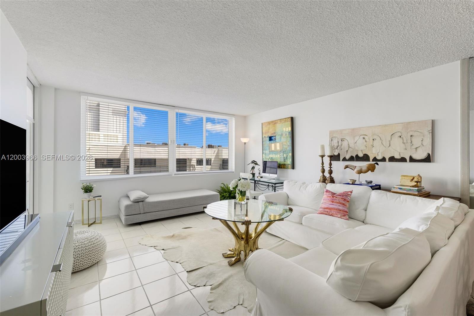 A bright living room features white tile floors, a white sectional sofa, and large windows — 5401 Collins Ave # 611, Miami Beach FL 33140, MIAMI BEACH, FL
