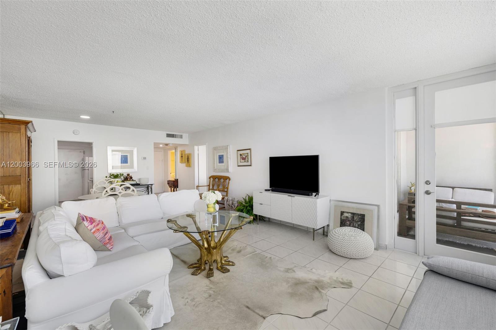 A bright living room features a white sectional sofa, glass-topped coffee table, and tiled floors — 5401 Collins Ave # 611, Miami Beach FL 33140, MIAMI BEACH, FL