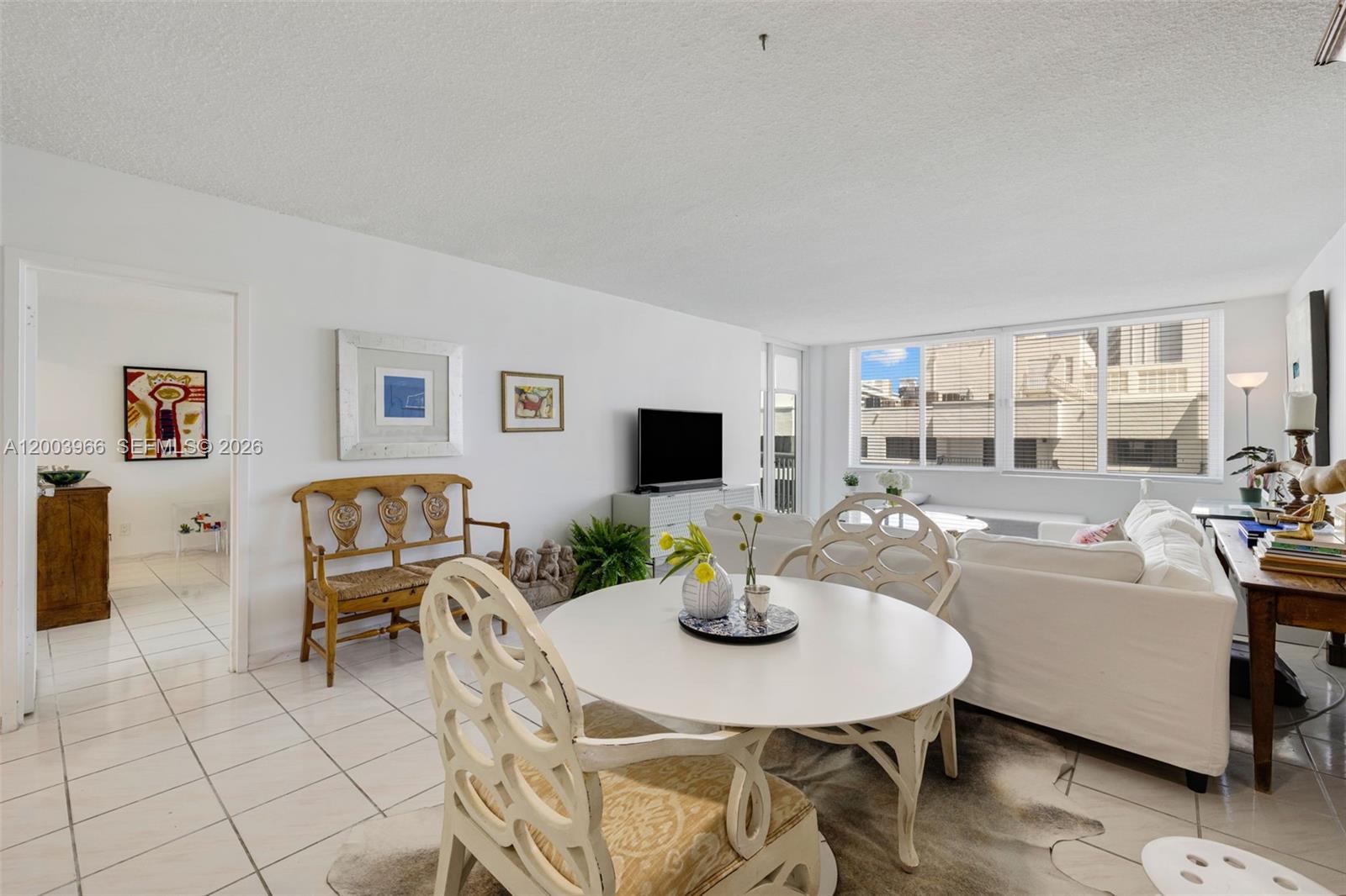 A bright living and dining area features white tile floors, white furniture, and large windows — 5401 Collins Ave # 611, Miami Beach FL 33140, MIAMI BEACH, FL