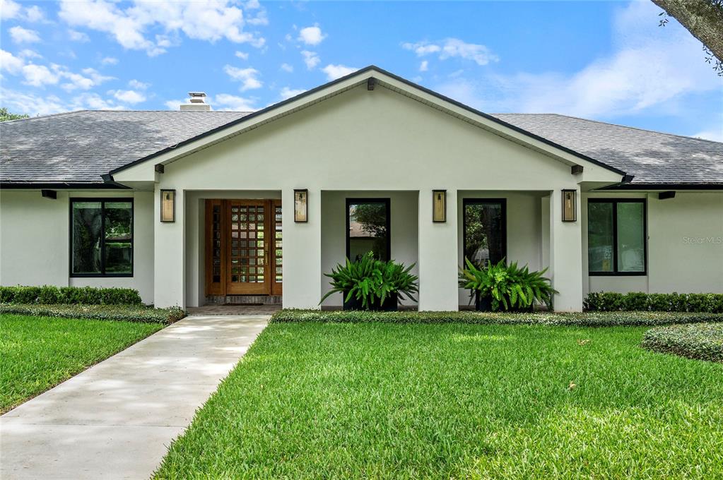 A single-story house with a white stucco facade, a wooden front door, and a lawn — 220 ADAMS DRIVE, MAITLAND, FL