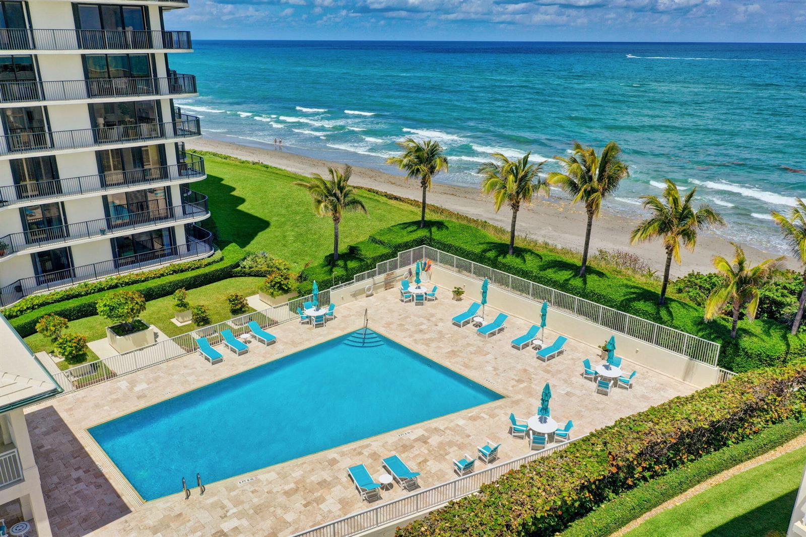 An aerial view of a rectangular swimming pool with lounge chairs and tables beside the ocean — 400 Beach Road # 103, Tequesta FL 33469, TEQUESTA, FL