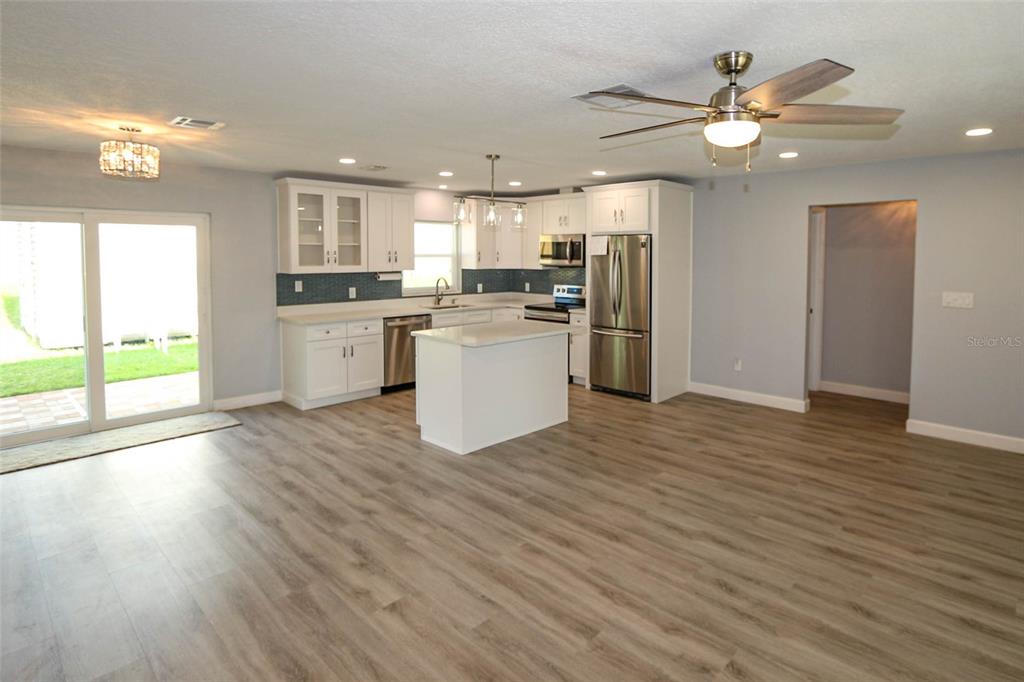 A kitchen with white cabinets, stainless steel appliances, and an island opens to a living area — 1444 OVERCASH DRIVE, DUNEDIN, FL