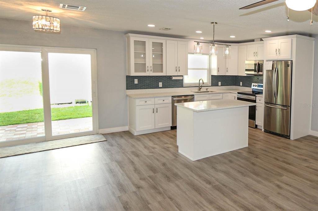 A modern kitchen features white cabinets, stainless steel appliances, a center island, and wood-look flooring — 1444 OVERCASH DRIVE, DUNEDIN, FL