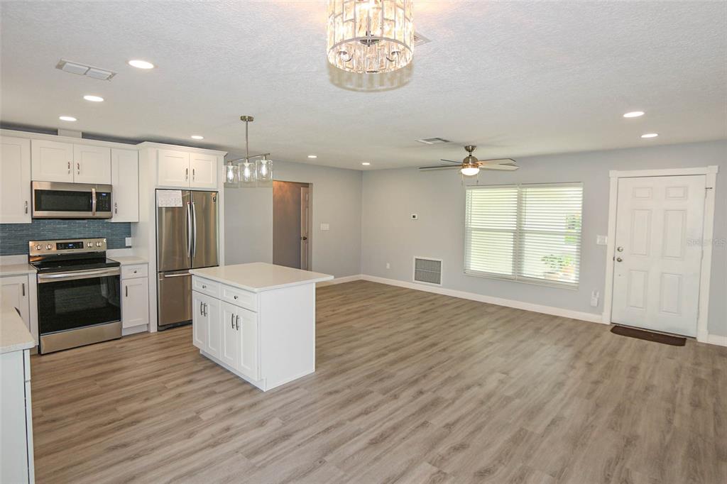 A kitchen with white cabinets, stainless steel appliances, and an island opens to a living area — 1444 OVERCASH DRIVE, DUNEDIN, FL