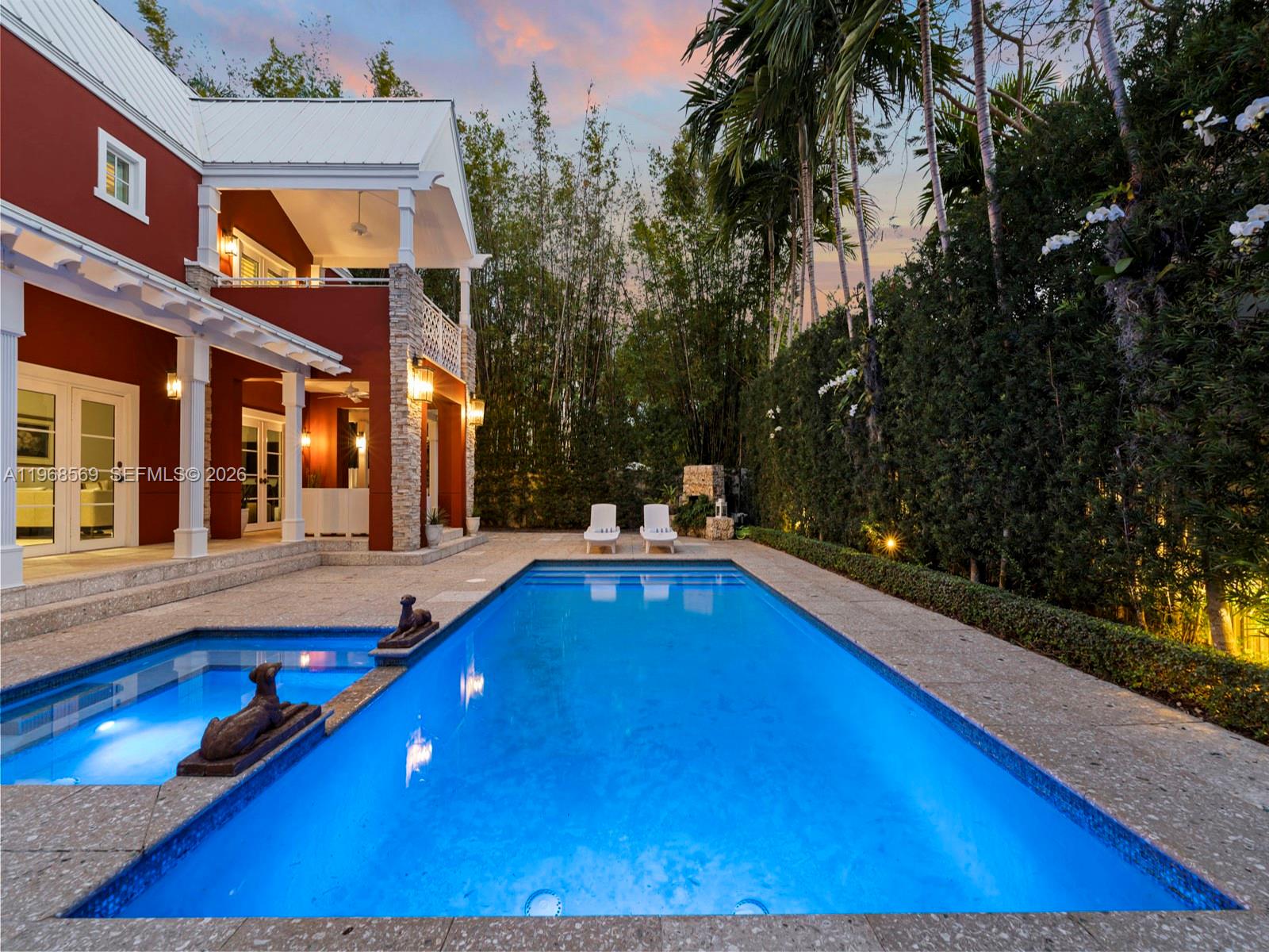 A swimming pool with a small attached spa sits beside a red house with palm trees — 7218 SW 54th court, Miami FL 33143, MIAMI, FL