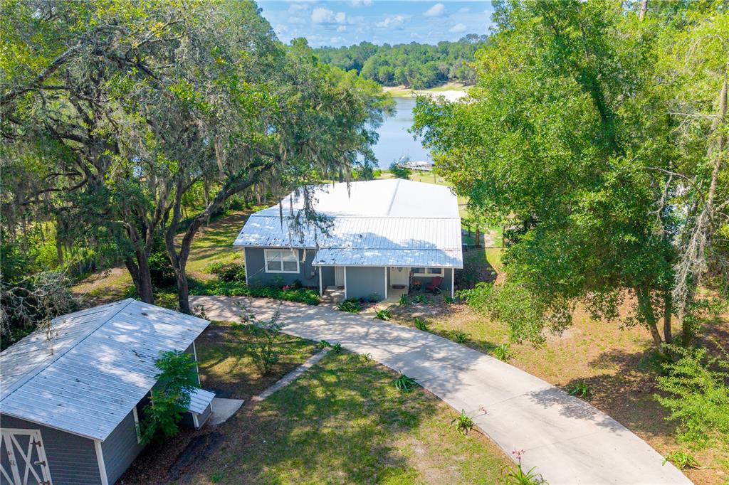 An aerial view shows a gray house with a white metal roof and a driveway — 7765 TWIN LAKES ROAD, KEYSTONE HEIGHTS, FL