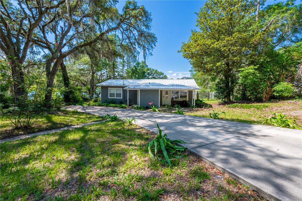 A gray single-story house with a metal roof sits at the end of a driveway — 7765 TWIN LAKES ROAD, KEYSTONE HEIGHTS, FL