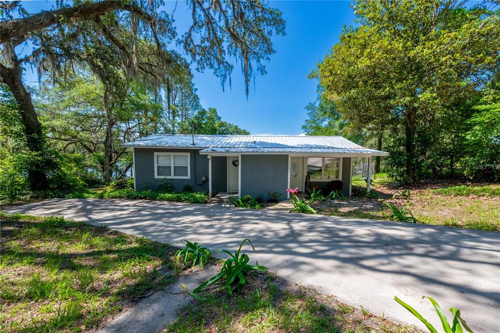 A single-story gray house with a metal roof sits behind a concrete driveway — 7765 TWIN LAKES ROAD, KEYSTONE HEIGHTS, FL