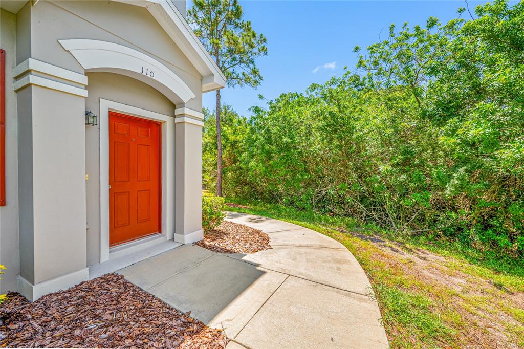 A bright orange front door is set into a beige exterior wall with a walkway — 10409 CRIMSON PARK LANE UNIT 110, TAMPA, FL
