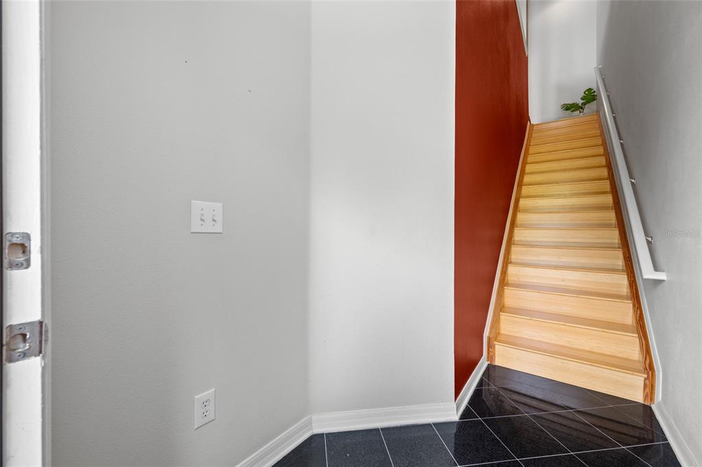 A staircase with light wood steps and a white railing sits beside a red wall — 10409 CRIMSON PARK LANE UNIT 110, TAMPA, FL