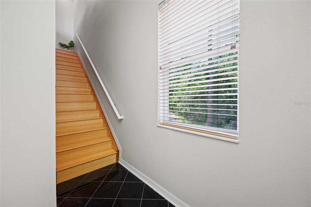 A staircase with light wood steps and a white railing sits beside a windowed wall — 10409 CRIMSON PARK LANE UNIT 110, TAMPA, FL