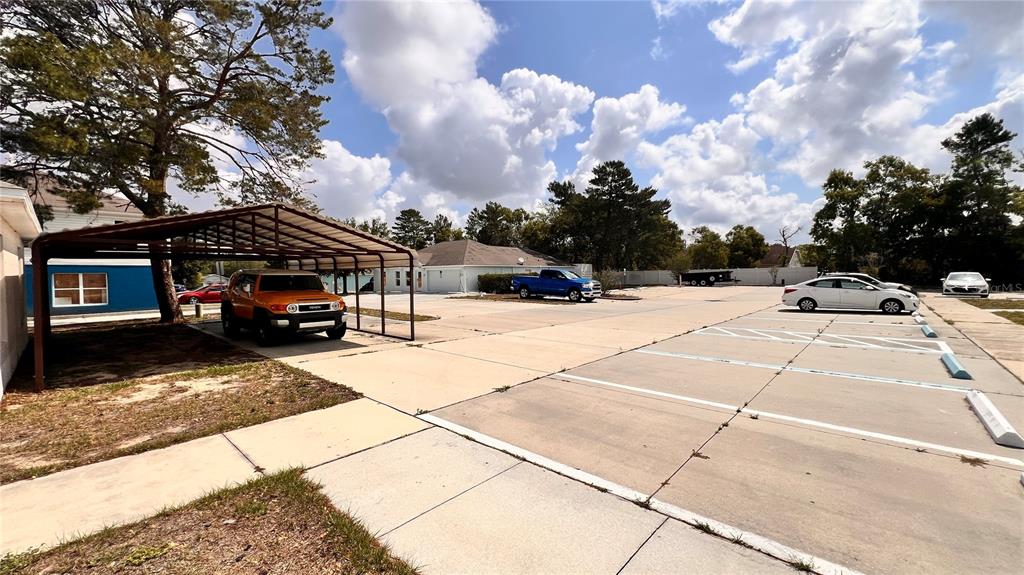 A parking lot features a metal carport covering an orange SUV and marked parking spaces — 3083 LANDOVER BOULEVARD, SPRING HILL, FL