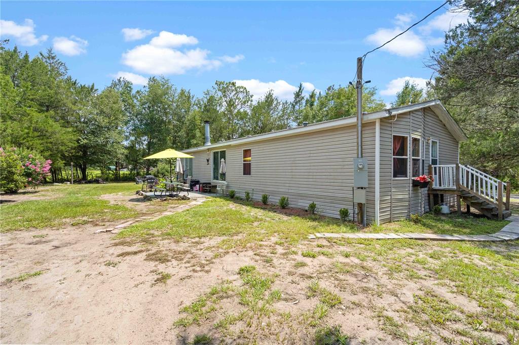 The exterior of a single-story beige house with a small wooden deck and patio area — 151 NE 164TH AVENUE, WILLISTON, FL