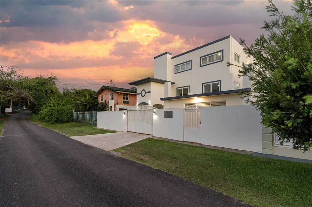A three-story modern house with a white exterior and gated driveway stands at sunset — SR 307 km 7.9 Boqueron VILLA NAUTICA, UNION ST, JOSE ST BEACH Lot # 2, BOQUERON, PR